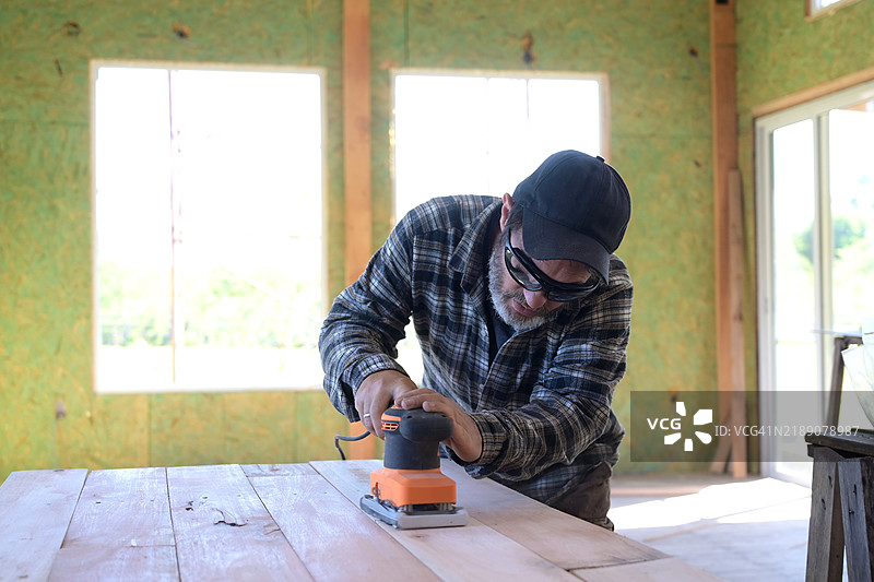 男子在木材上使用圆盘砂光机。图片素材