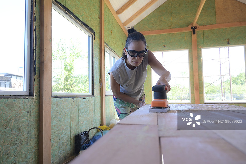 女性在木材上使用圆盘砂光机。图片素材