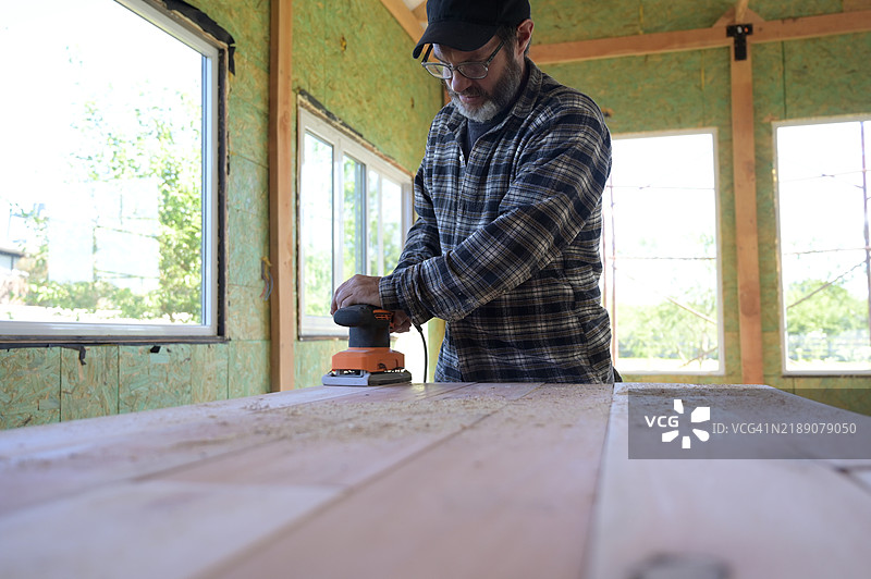男子在木材上使用圆盘砂光机。图片素材