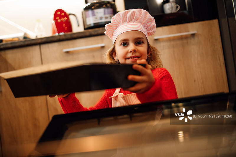 女孩厨师从烤箱中取出饼干。图片素材