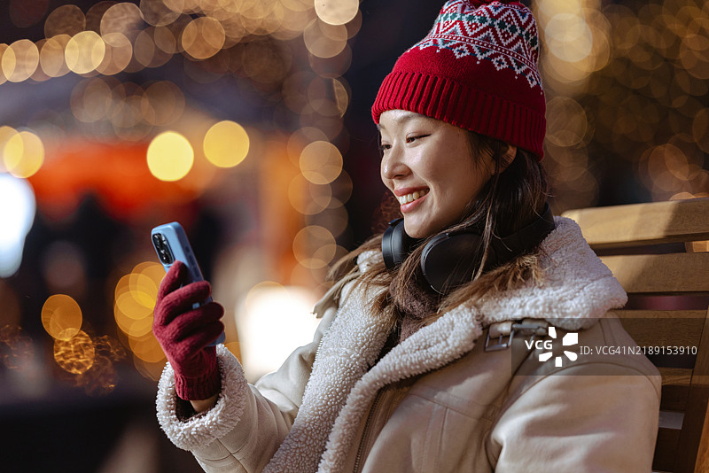 女人在户外享受圣诞冬季夜晚，手里拿着智能手机图片素材