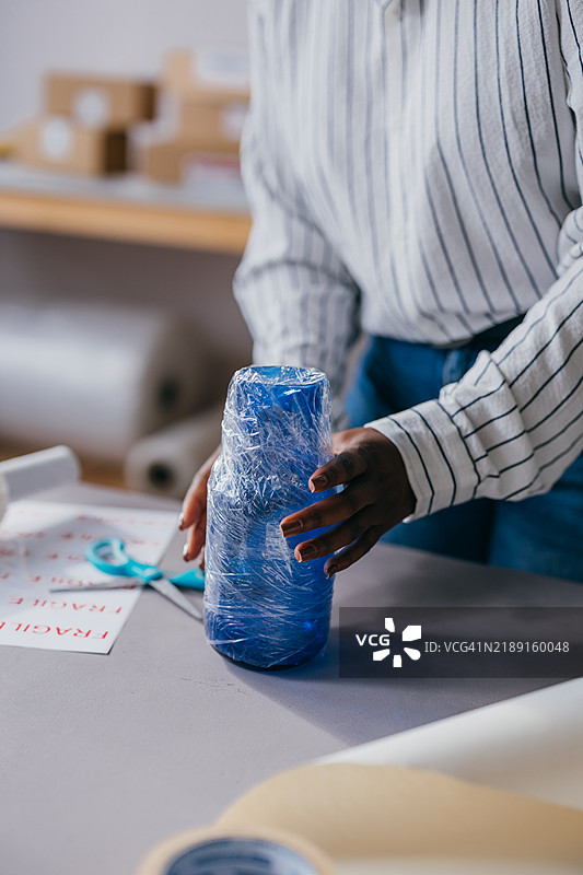 在包装区用塑料包裹蓝色瓶子的人图片素材