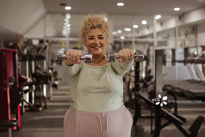 健身自信：一位丰满女性自信地举着哑铃锻炼图片素材