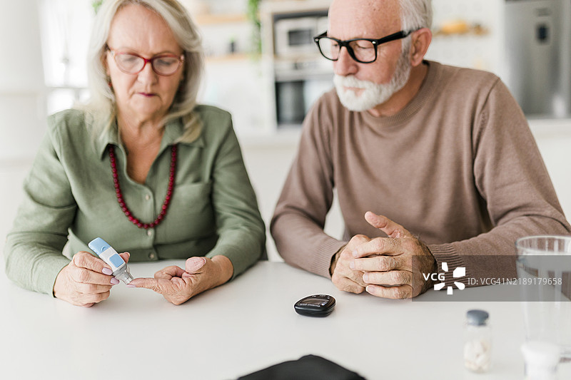 老年夫妇使用刺血针在手指上检查血糖水平，血糖仪，医疗保健和医学，糖尿病，血糖概念图片素材