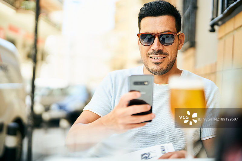年轻男子在酒吧喝啤酒时使用手机图片素材