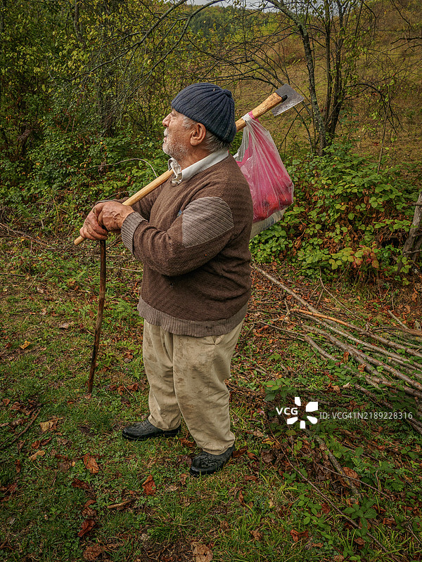 侧面视图的老年男子在田野上站着，手持拐杖。图片素材