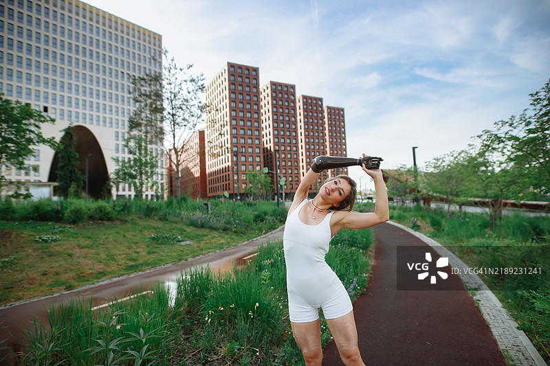 城市早晨日常：女性在现代城市高楼附近的公园里热身和拉伸。图片素材