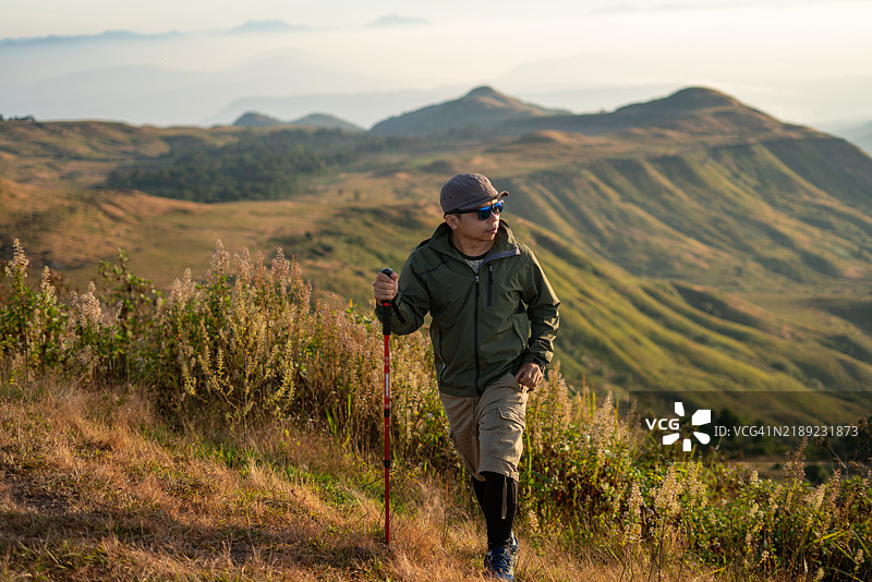 穿着绿色夹克的冒险登山者在日出时探索山地风景图片素材