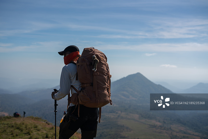 背包客手持登山杖和大背包在阳光明媚的山地风景中徒步旅行图片素材