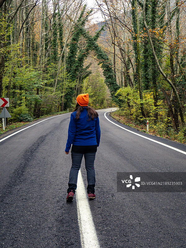 背影女性站在道路上，身后是树木。图片素材