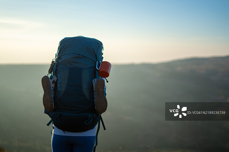 背包客在日出时俯瞰风景如画的山谷，身旁有登山装备图片素材
