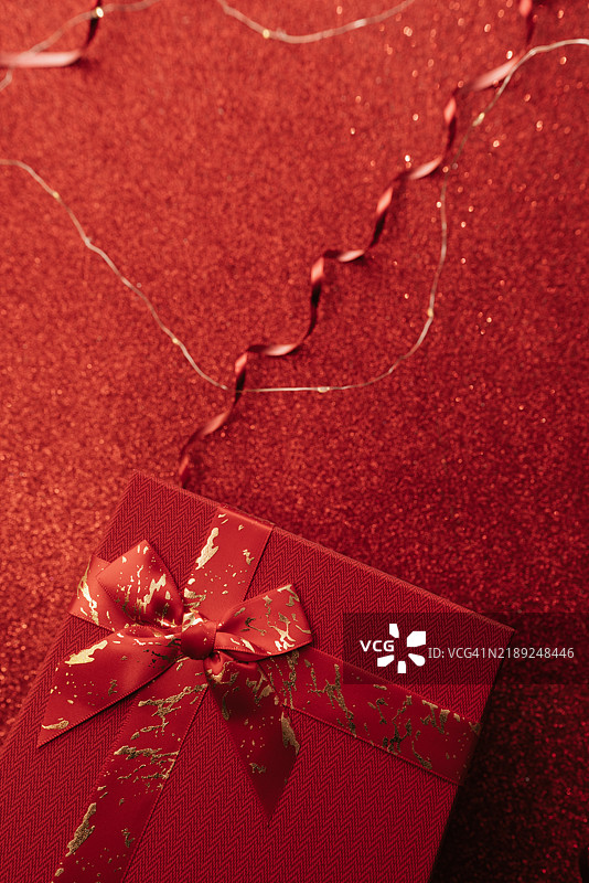 一个精美包装的黑色礼品盒，装饰着鲜艳的红色丝带，坐落在充满心形图案的闪亮红色背景上，非常适合在情人节庆祝爱情。图片素材