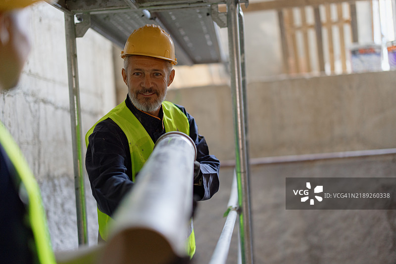 建筑工人在工地上佩戴安全装备搬运管道图片素材