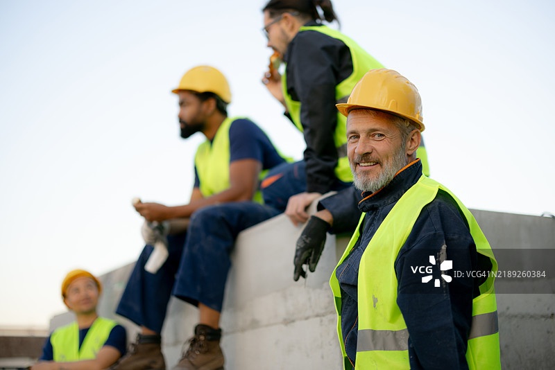 微笑的建筑工人在安全装备下在工地上休息图片素材