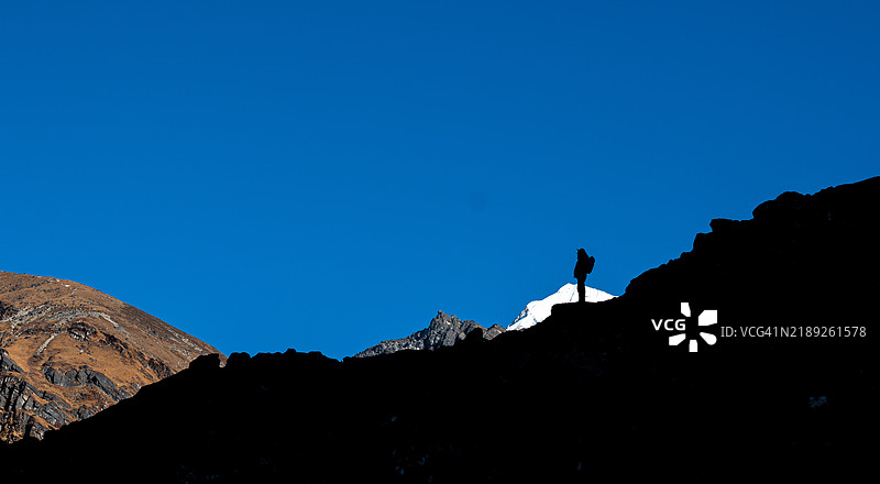 低角度视图下，山顶上站着的男人剪影，背景是晴朗的蓝天。图片素材