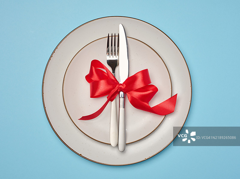 圆形白色盘子上系着红色丝带，旁边有刀具，背景为黄色，节日餐桌布置图片素材