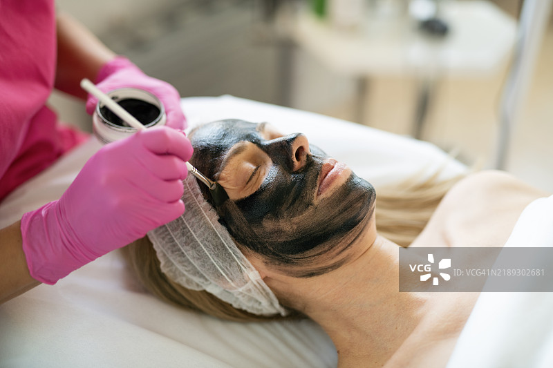 在美容水疗中心为女性面部涂抹面膜的特写镜头。图片素材