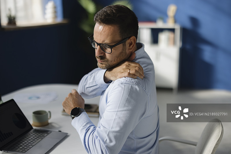 不满的商人在办公室感到肩膀僵硬。图片素材