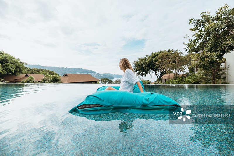 女人在无边泳池中放松，坐在漂浮的豆袋椅上。图片素材