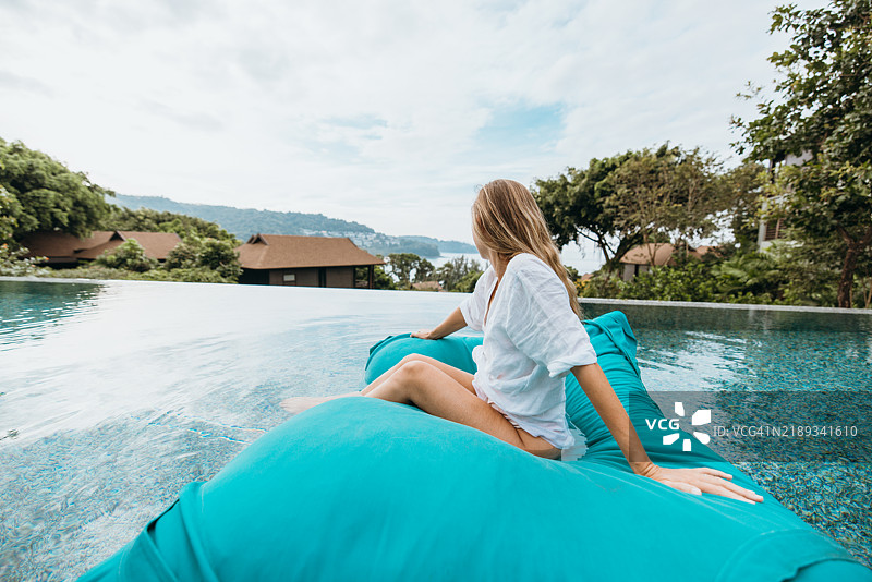 女人在无边泳池中放松，坐在漂浮的豆袋椅上。图片素材