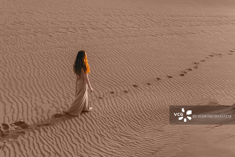 美丽的年轻红发女性在沙漠地区的日落光线下。图片素材