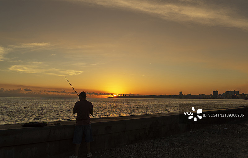 古巴。哈瓦那。日落时分，一个人在马雷孔钓鱼的剪影。图片素材