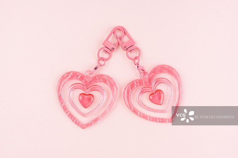 粉色背景上的两个粉色心形钥匙扣。图片素材