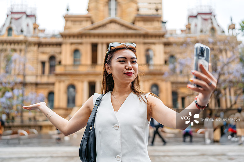 年轻亚洲女性在澳大利亚悉尼市政厅附近用手机自拍图片素材