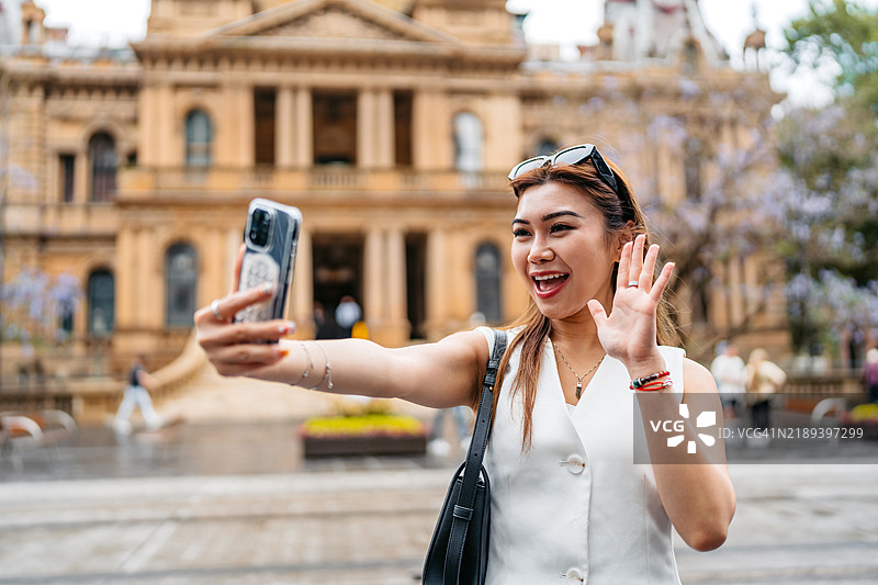 年轻亚洲女性在澳大利亚悉尼市政厅附近使用手机进行视频通话图片素材