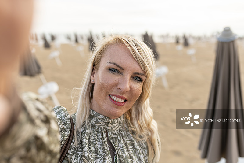 女人在空旷的海滩上拍自拍，周围有关闭的伞。图片素材