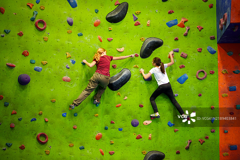 室内攀岩初学者 - 两位年轻攀岩者在色彩斑斓的墙面上图片素材