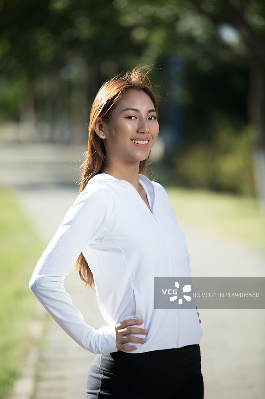 微笑的亚洲女性穿着运动服，双手叉腰站立。图片素材