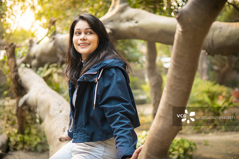 愉快放松的年轻女性坐在倒下的树上，享受大自然中的新鲜空气。图片素材