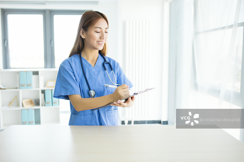 亚洲女性医生在医院的夹板上写字图片素材