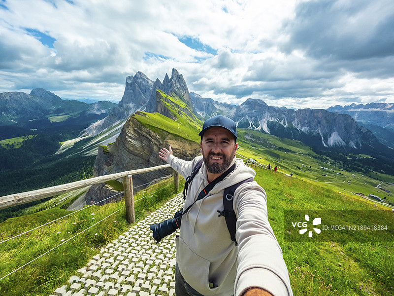 背着背包和相机的摄影师，伸出手臂自拍，背景是奥多尔山脉群。图片素材