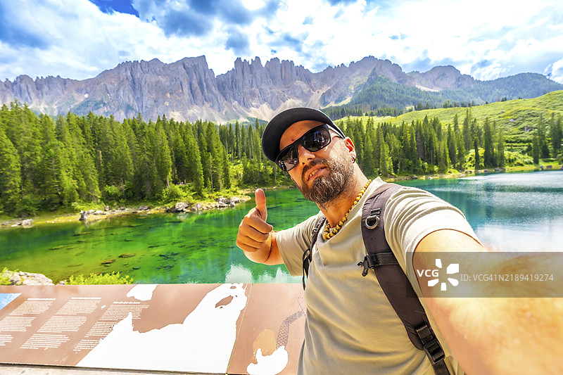 游客在卡雷扎湖和多洛米蒂山脉的壮丽景色中享受自拍并竖起大拇指。图片素材