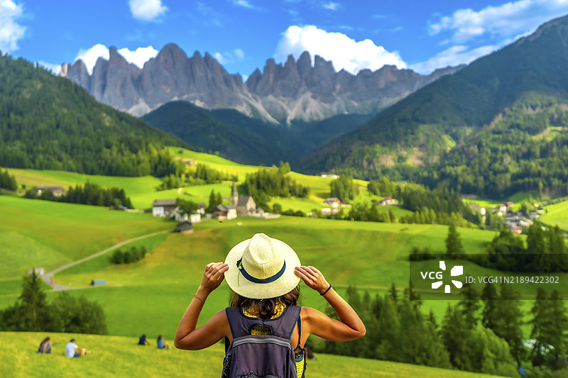女性游客手持帽子，凝视着位于芬斯谷的圣玛德琳娜教堂，背景是奥德尔山脉。图片素材