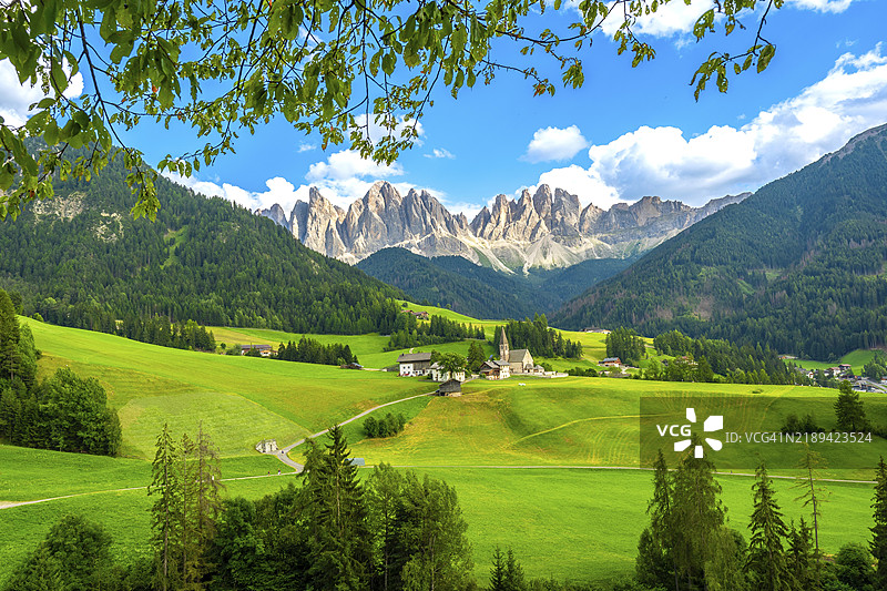 圣马达莱纳教堂的框架下,绿色的草地和树木突显了瓦尔迪芬斯的壮丽夏日景象,背景是雄伟的奥德尔山脉。图片素材