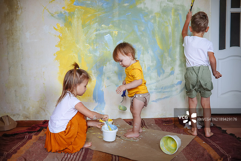 孩子们与创造力：三个兄弟姐妹在墙上绘画，为装修过程增添色彩和乐趣。图片素材