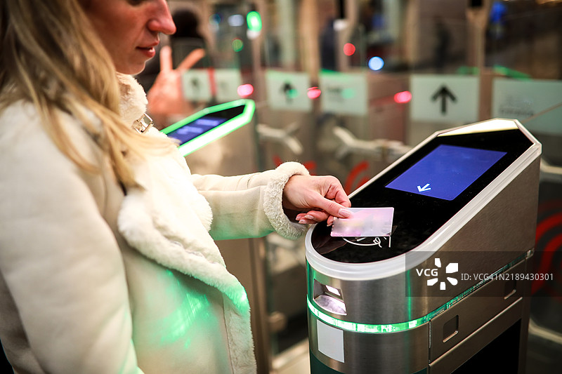 冬季通勤：年轻女性使用卡片支付地铁通行费，展示现代无接触支付方式。图片素材