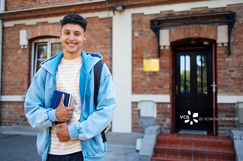 快乐的学生站在学校建筑外，手里拿着书籍图片素材