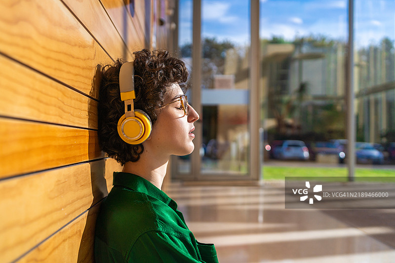 宁静的时刻：年轻女性戴着耳机，闭着眼睛在现代可持续办公室中享受音乐图片素材