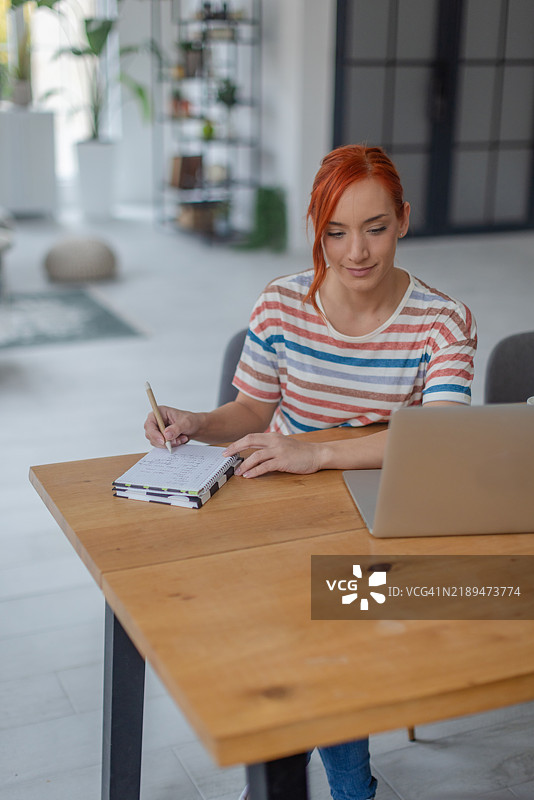 年轻女性在书桌前学习，使用笔记本电脑和笔记，专注于学习图片素材