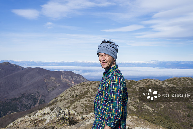 登山者站在山顶，享受美景并朝着镜头微笑。图片素材