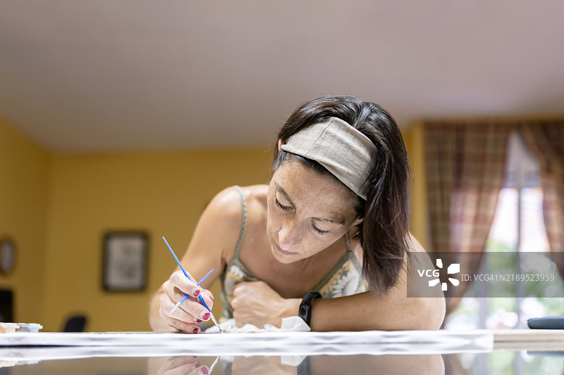 戴着头带的女艺术家在工作桌后用画笔作画。图片素材