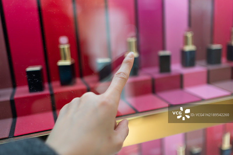 用手指触碰玻璃柜中的口红。图片素材