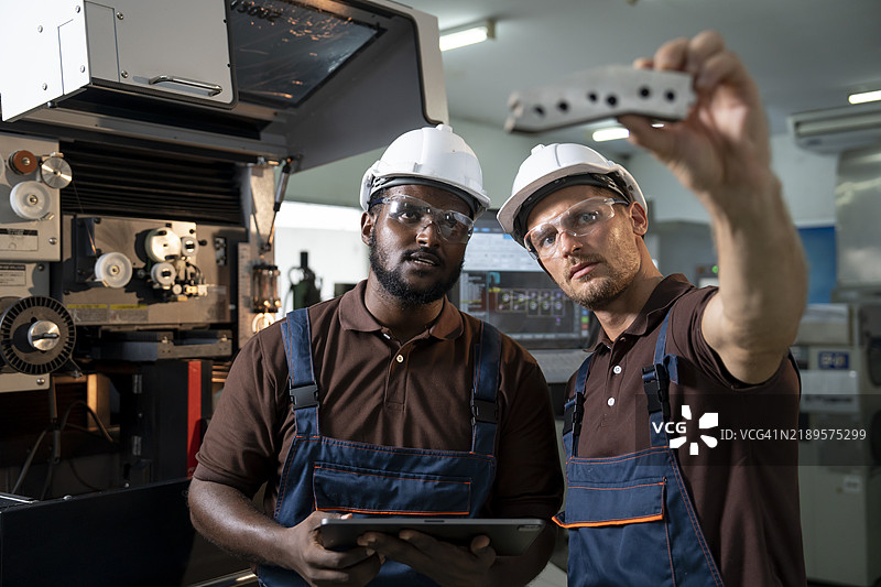 两名穿着安全装备的制造工程师讨论在工厂中使用数控机床的计划。图片素材