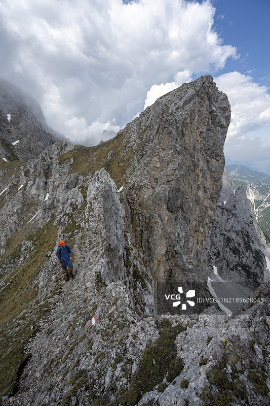 戴着头盔的登山者在崎岖的山脊狭窄小径上，攀登毛克斯皮策，云雾环绕着山脉，背景是阿克尔皮策，维尔德凯瑟，凯瑟山脉，奥地利，蒂罗尔，欧洲图片素材