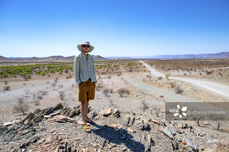 年轻男子站在山丘上，干旱贫瘠的地貌与丘陵，达马拉兰，库内内，纳米比亚，非洲图片素材
