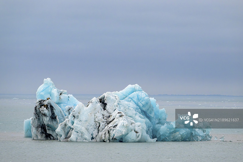 一座蓝白相间的冰山漂浮在平静的海面上，灰色的天空下，阿拉斯加，美国，北美。图片素材